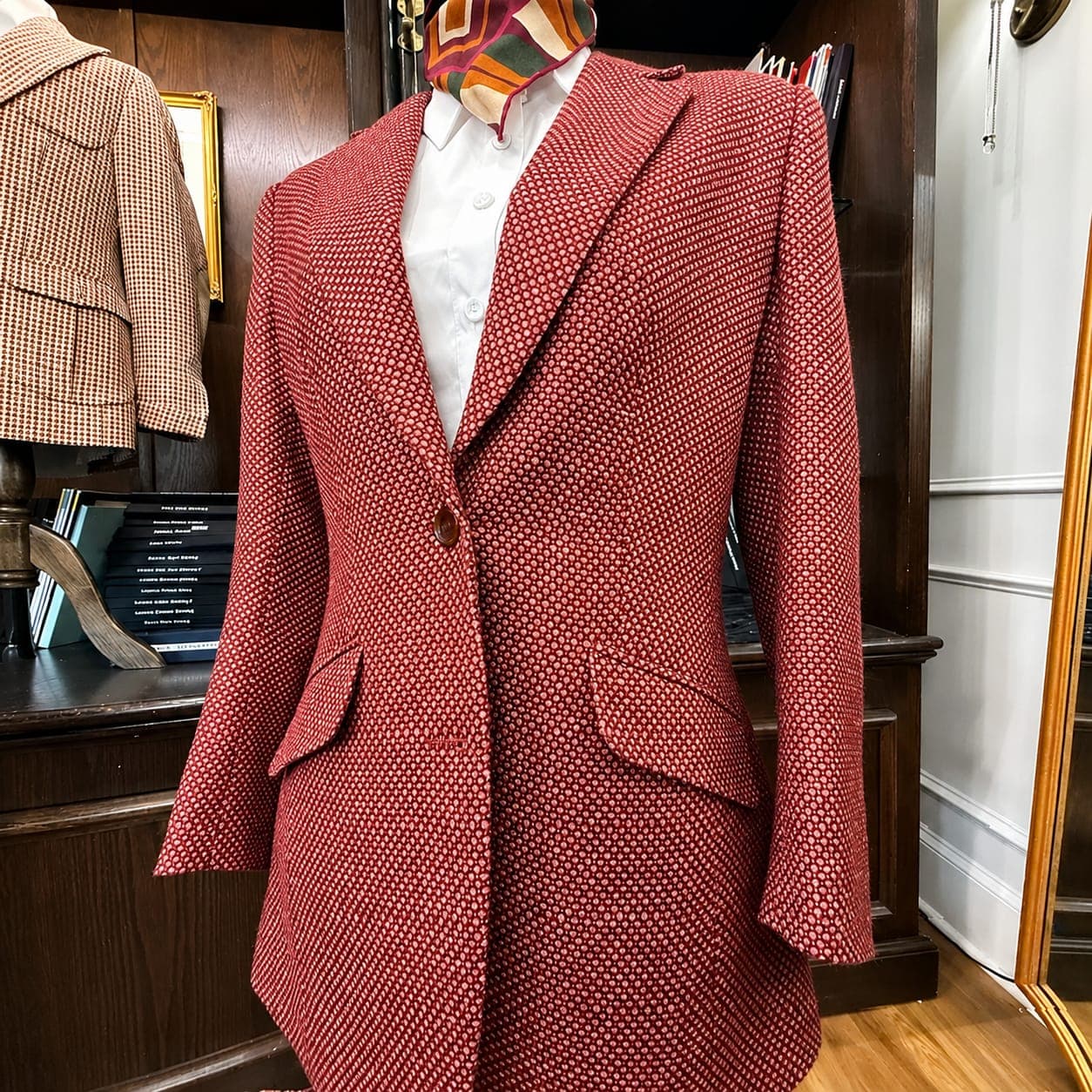 A deep red patterned women's jacket on a stand in the workroom